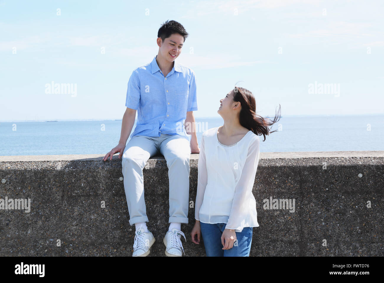 Young Japanese couple sitting on concrete wall by the sea Stock Photo ...