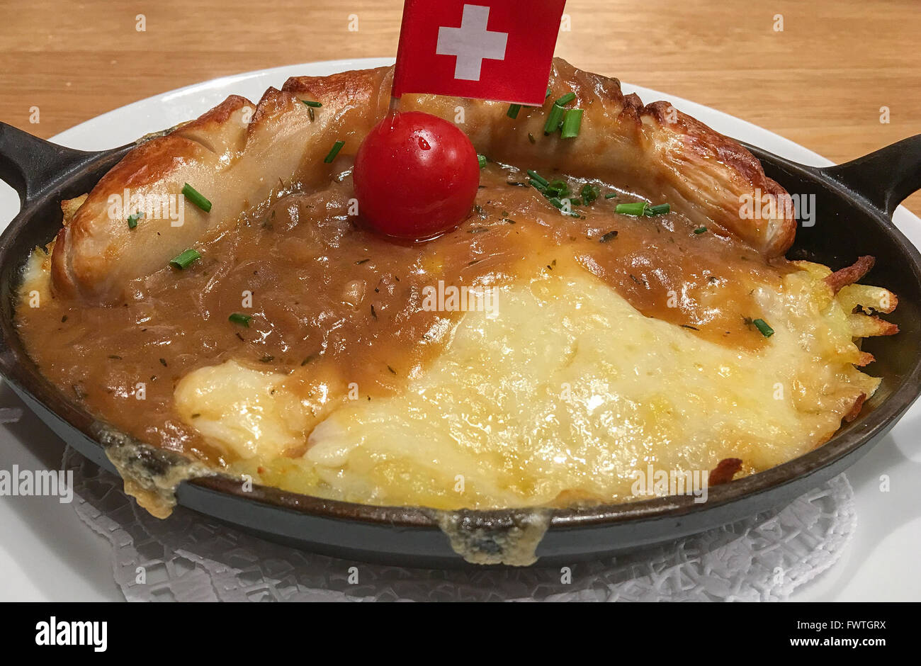 Traditional Swiss dinner of a veal sausage with potato rosti covered in melted cheese Stock Photo