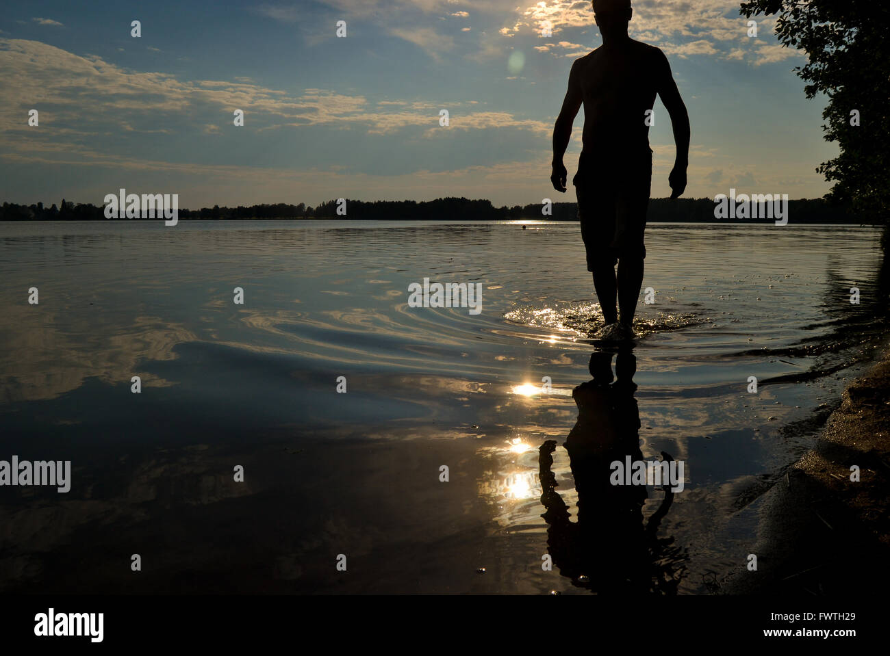 Man walking in the water by the lake in summer evening Stock Photo