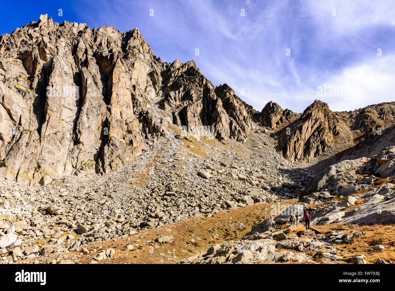 Hikers walk at the bottom of high rocky cliff. Stock Photo