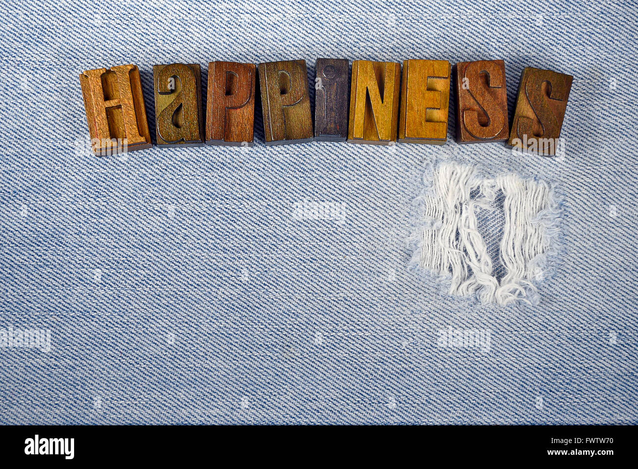 Word happiness in vintage letterpress type on frayed denim fabric. Stock Photo