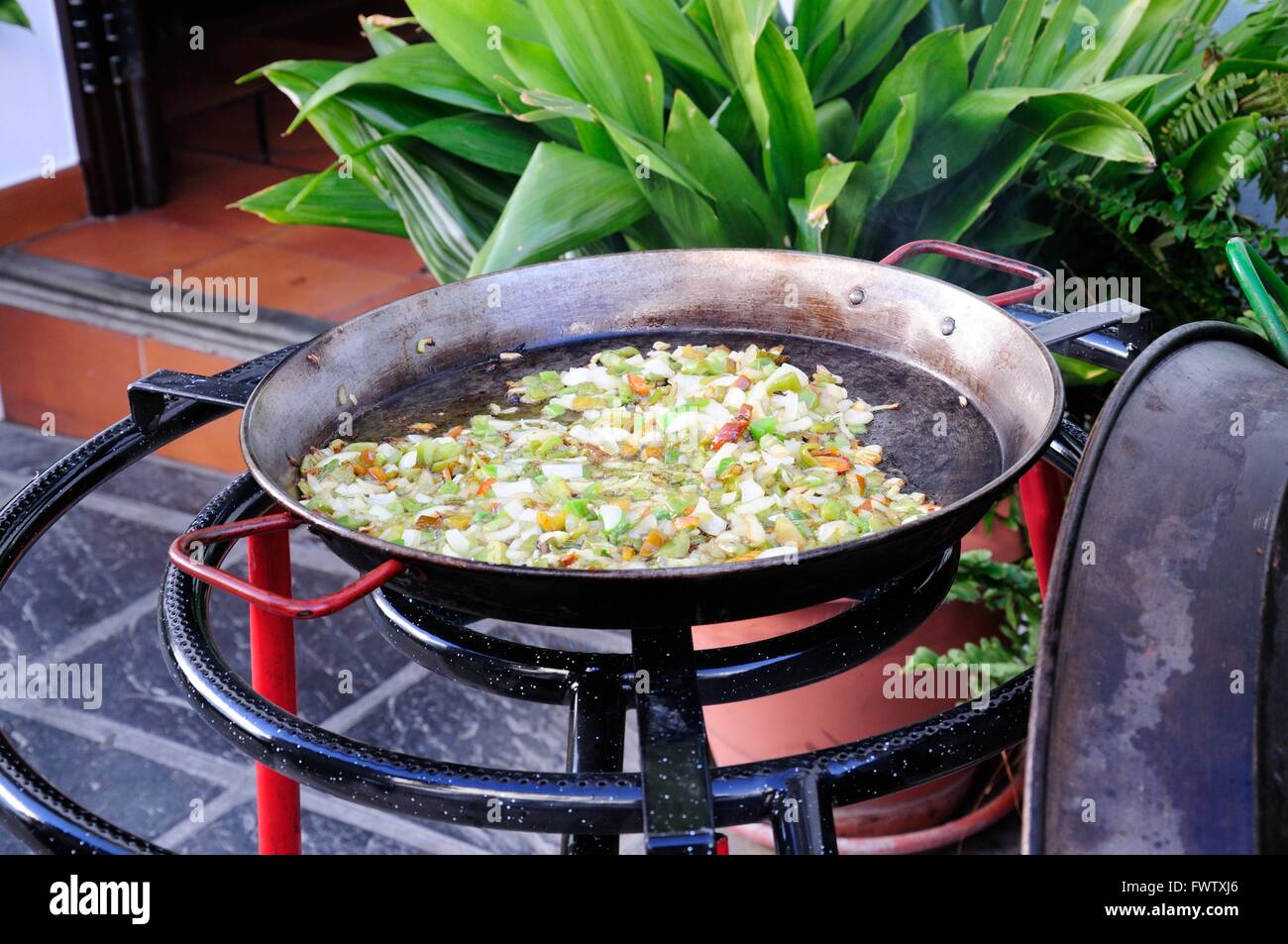 paella base onions garlic and peppers cooking outside in a paella pan