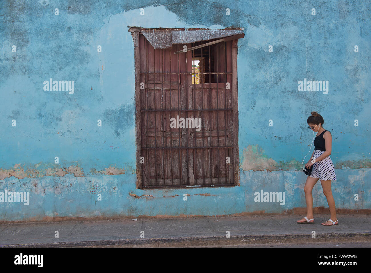 A woman walks past a wall of different colors and textures in the old Cuban town of Trinidad. Stock Photo