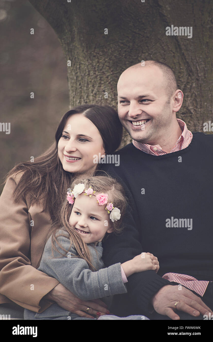 happy young parents sitting with their small daughter by the tree in park Stock Photo