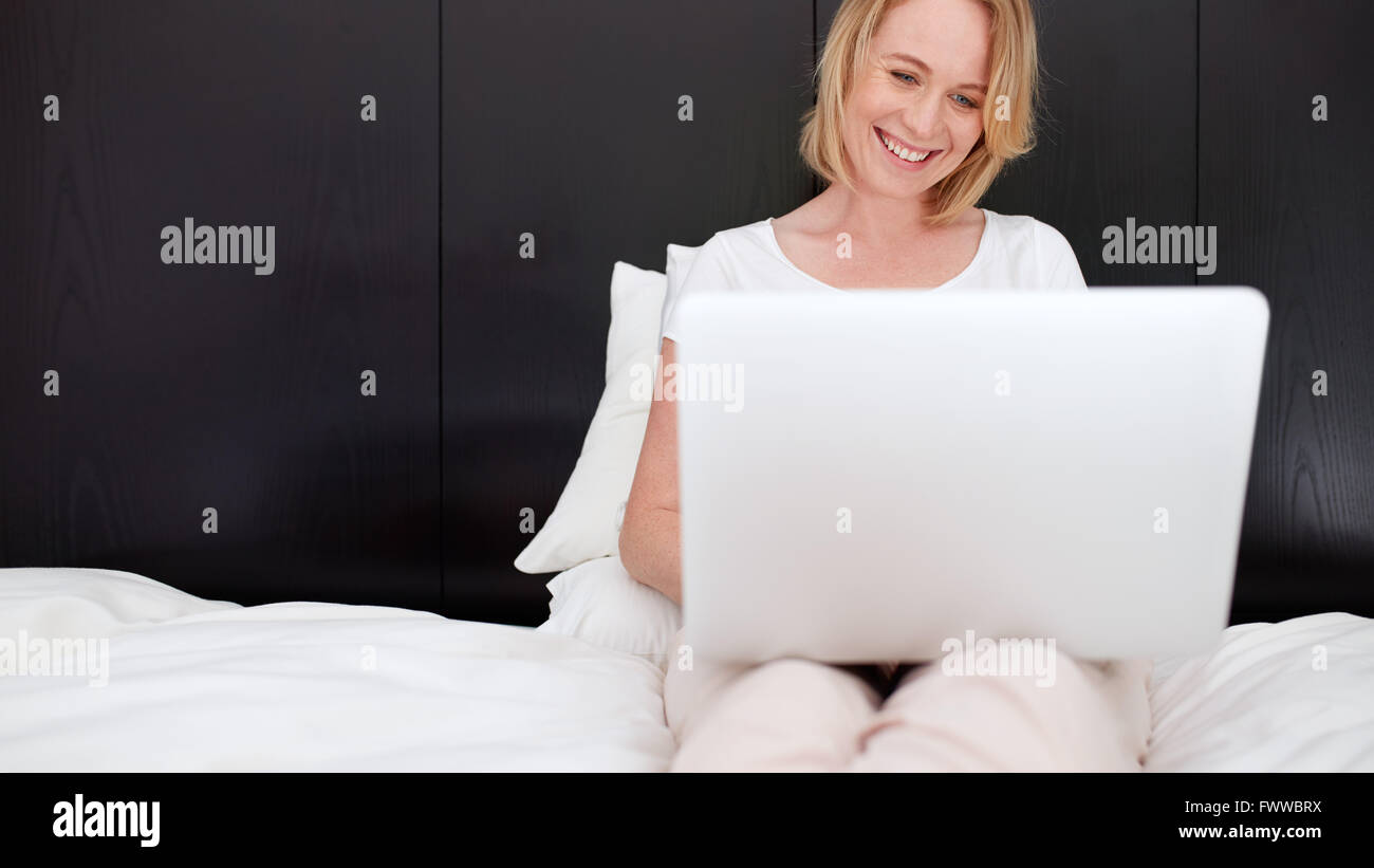 Portrait of happy mature woman sitting on bed and using laptop. caucasian woman relaxing in bedroom and surfing internet on her Stock Photo