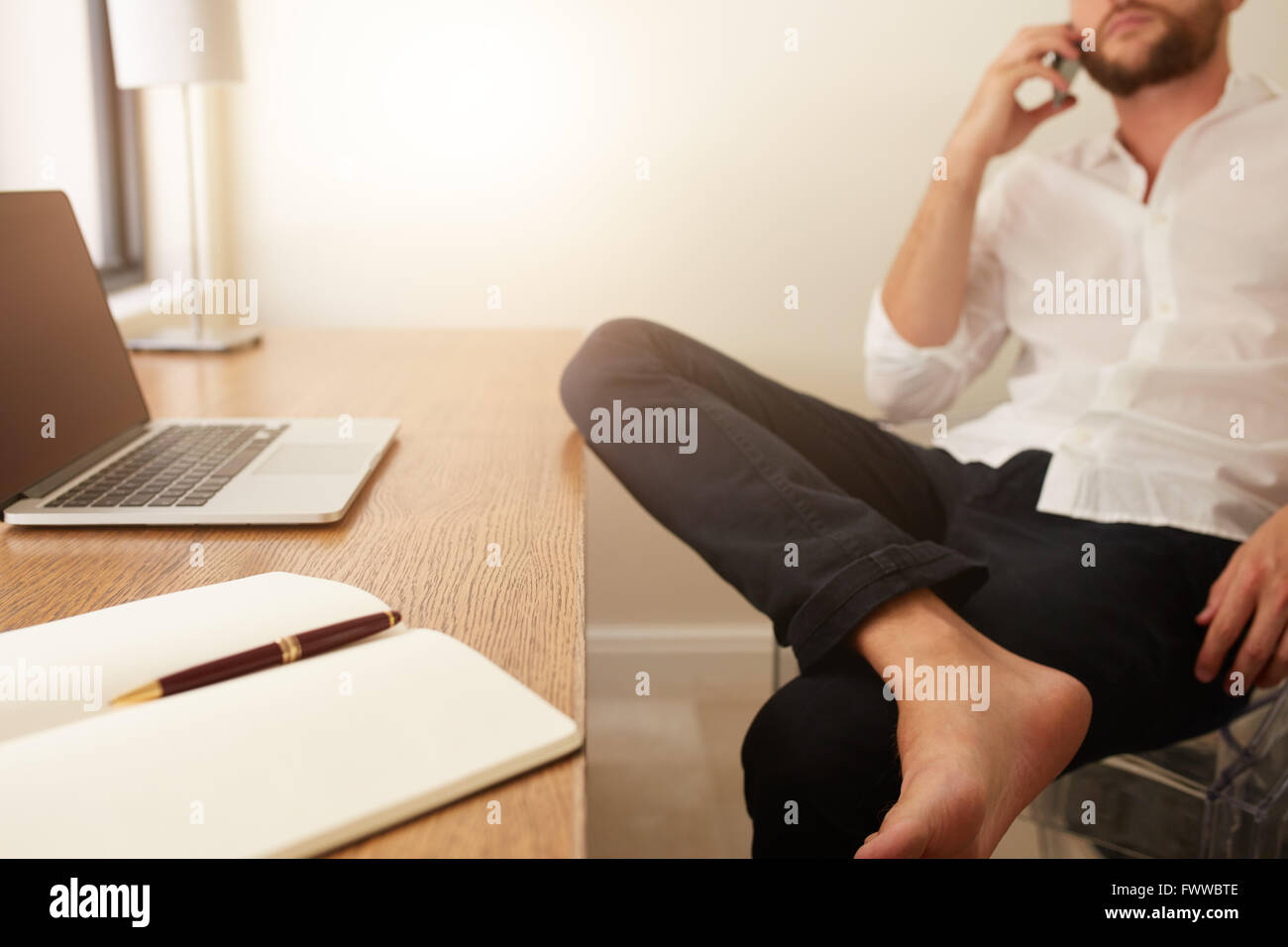 Diary and laptop on desk with businessman sitting in background making a phone call. Home office worktable. Stock Photo