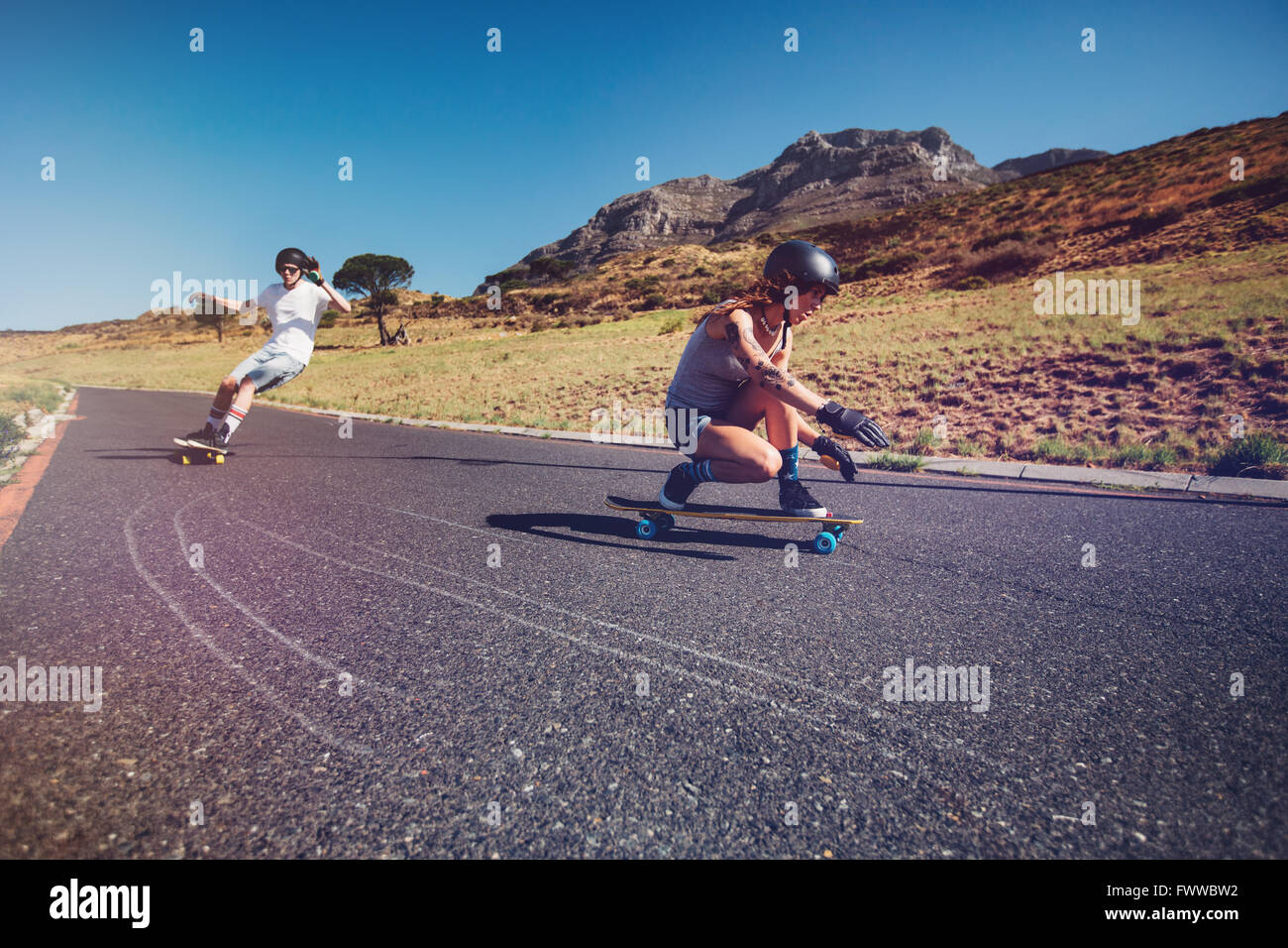 Two young people practicing long board riding outdoors on rural road. Man and woman longboarding on a summer day. Stock Photo