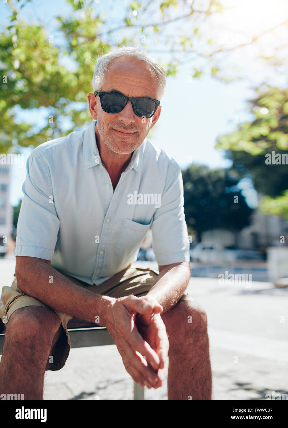 Portrait of handsome mature man sitting outdoors. Senior male tourist with sunglasses sitting outside in the city on a summer da Stock Photo