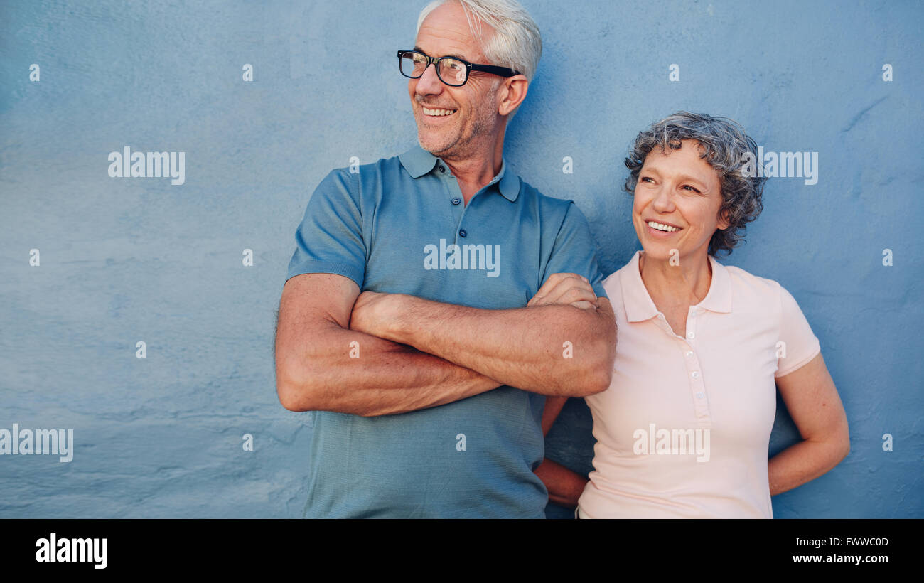 Portrait of a mature couple standing together and looking away and smiling against blue background. Middle aged man and woman le Stock Photo