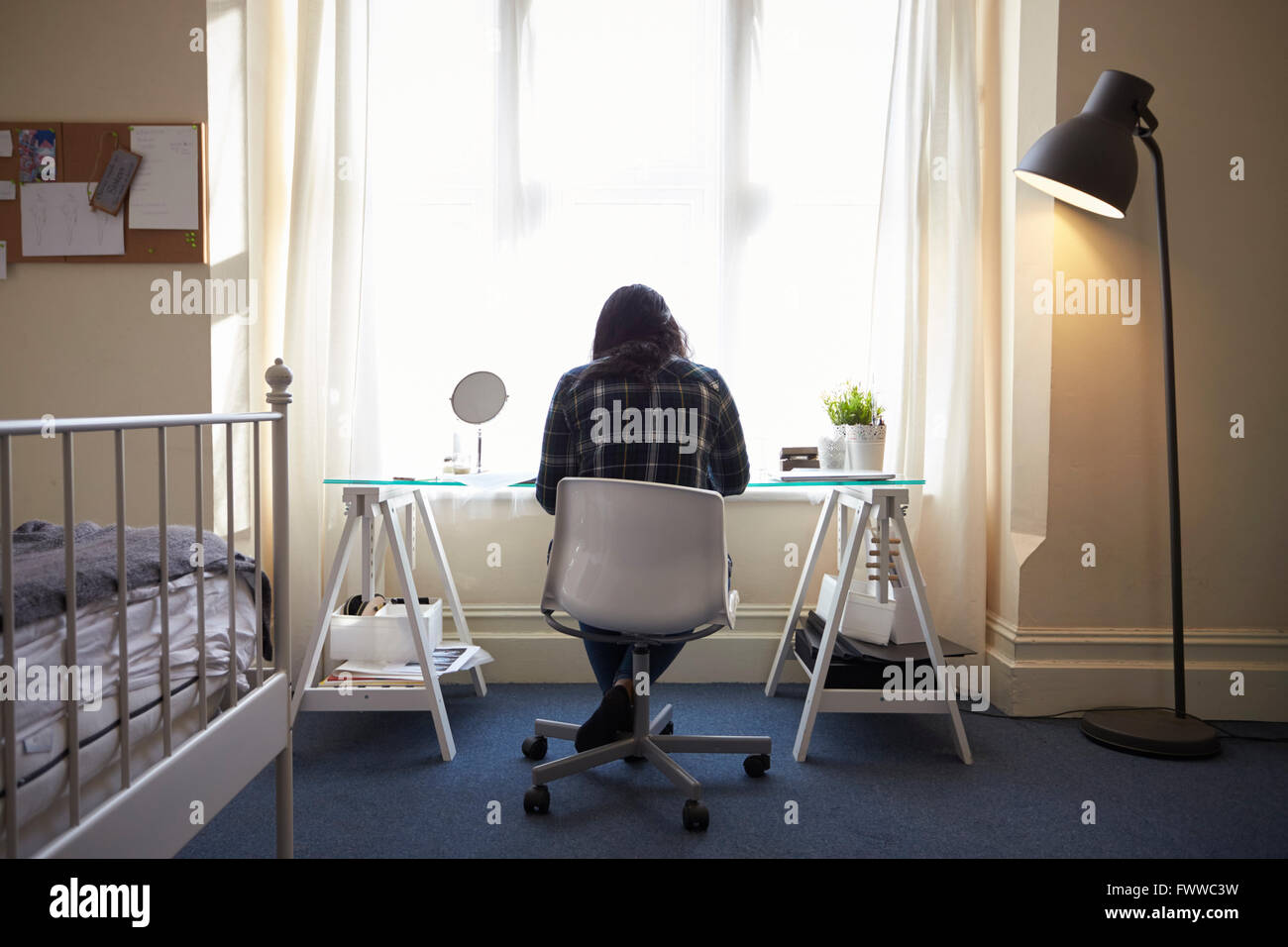 Female Student Sitting At Desk And Working In Bedroom Stock Photo