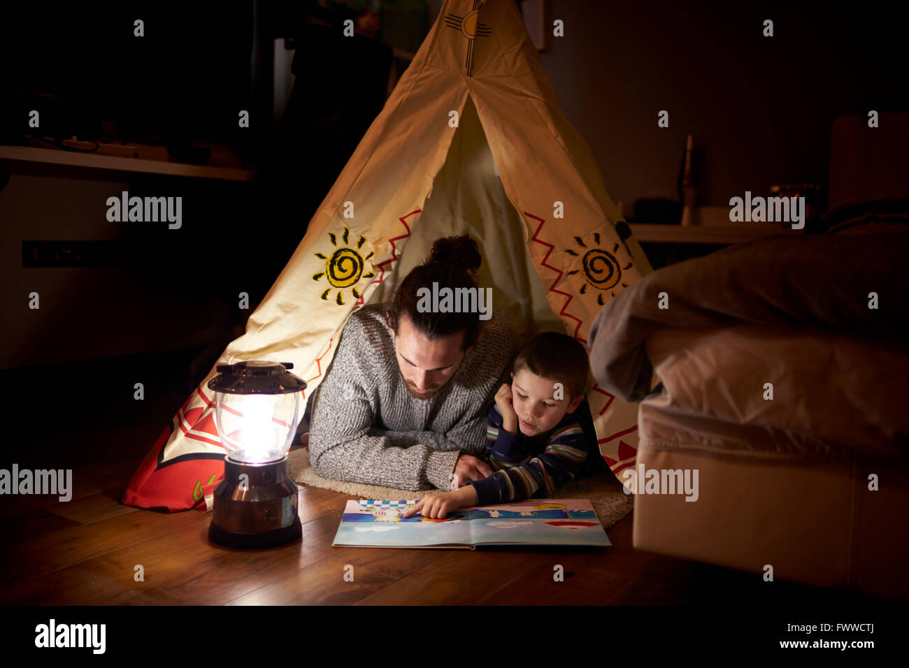 Father And Son Reading Inside Tent Set Up Indoors Stock Photo