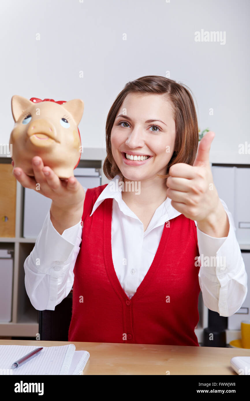 Happy business woman holding thumbs up with piggy bank in the office ...