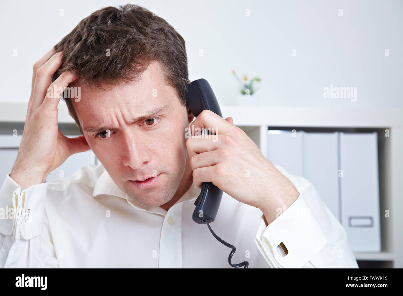 Frustrated business man waiting on the phone in a hotline queue Stock