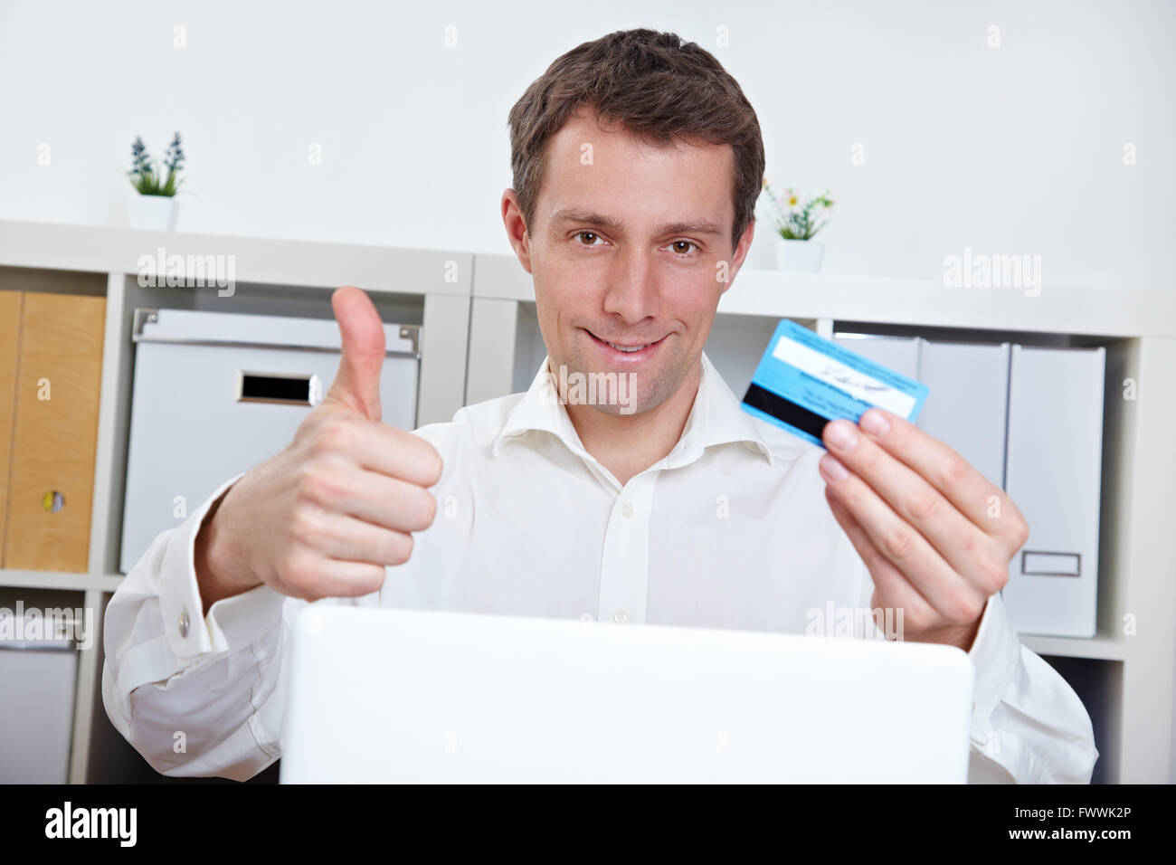 Happy business man with credit card holding thumbs up in the office Stock Photo