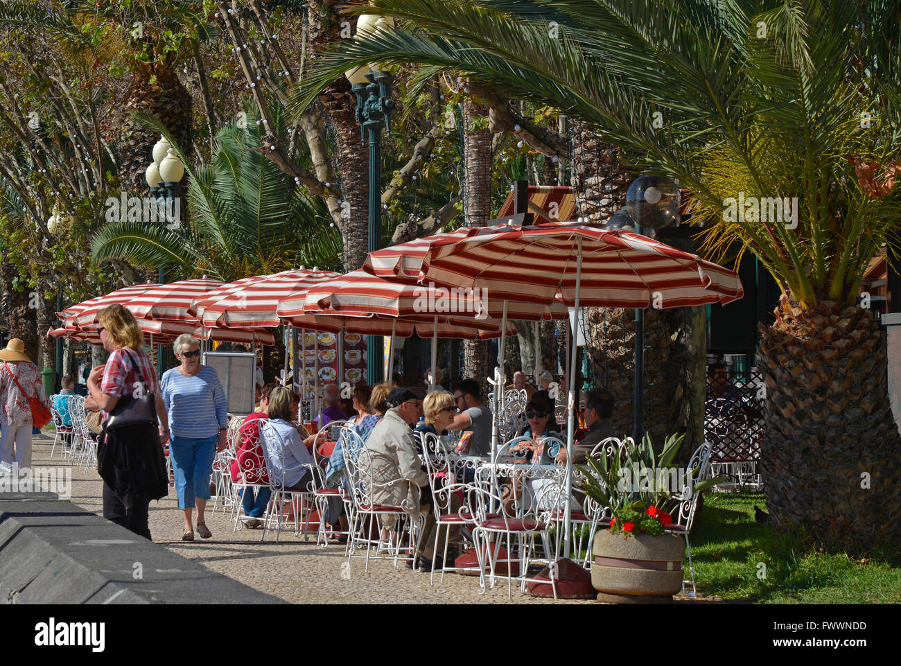 Cafe and restaurant with people sitting and strolling on seafront promenade in Funchal, Madeira, Portugal Stock Photo