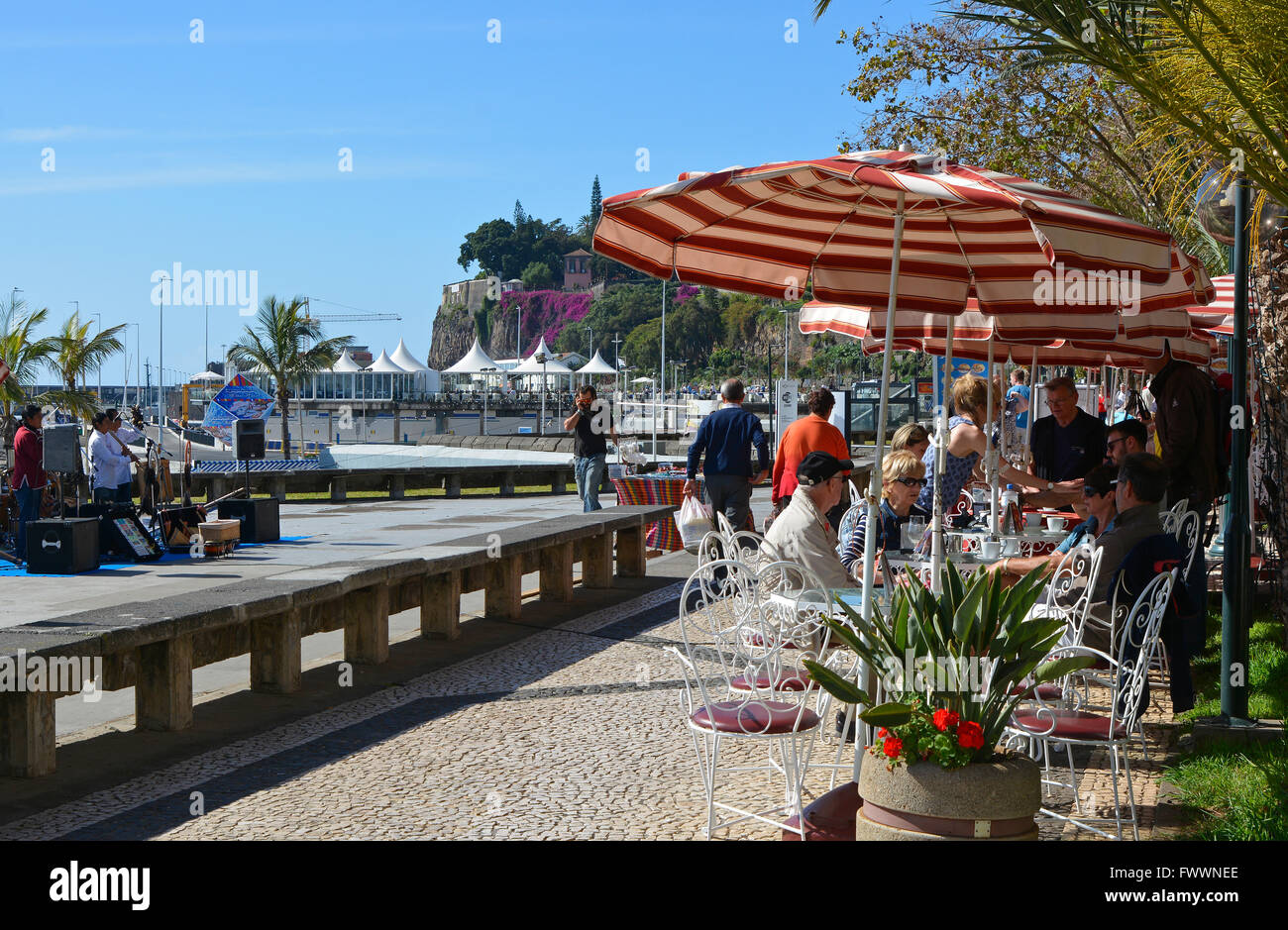Cafe and restaurant with people sitting and strolling on seafront promenade in Funchal, Madeira, Portugal Stock Photo