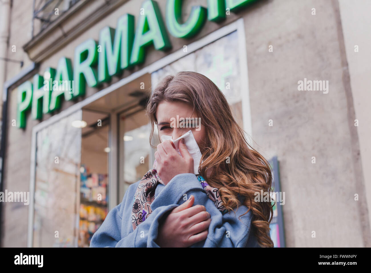 sick cold woman next to a pharmacy, flu concept, buy medicaments Stock Photo