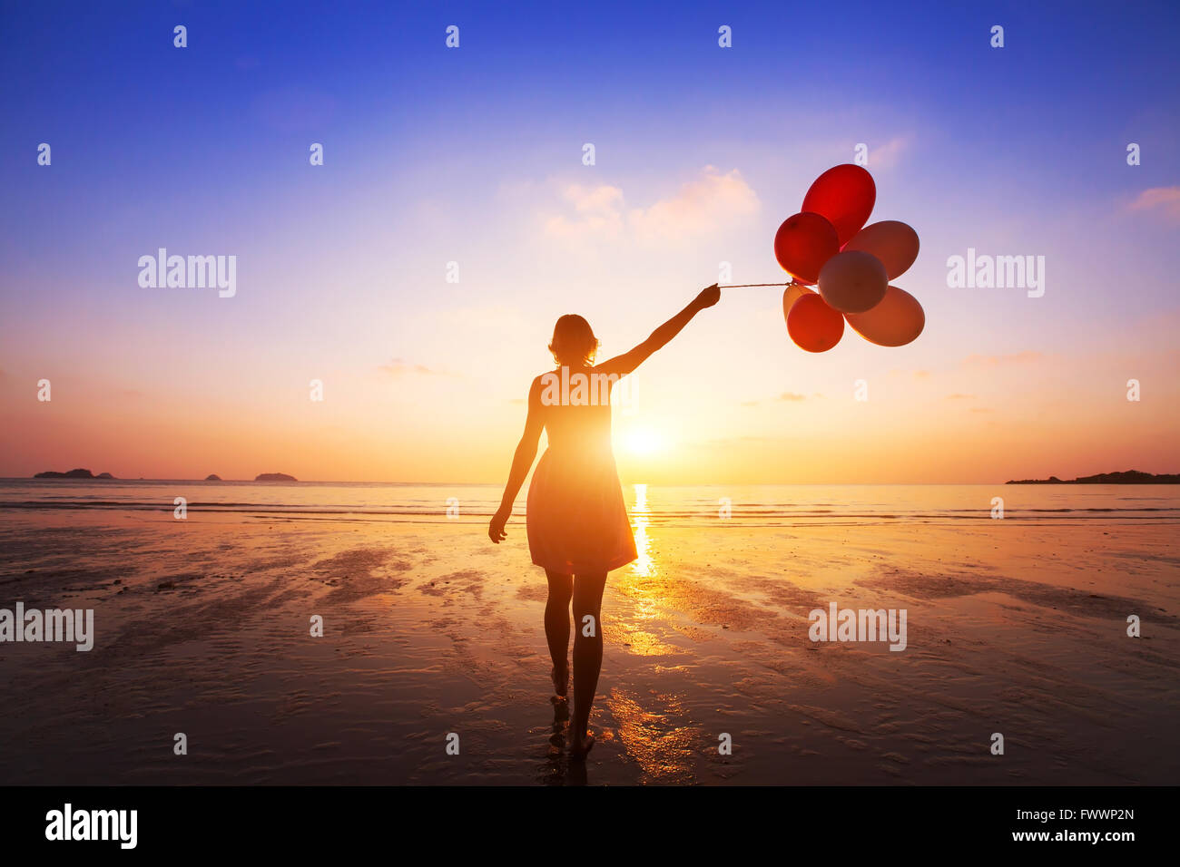 happiness concept, positive emotions, happy girl with multicolored balloons enjoying summer beach at sunset Stock Photo