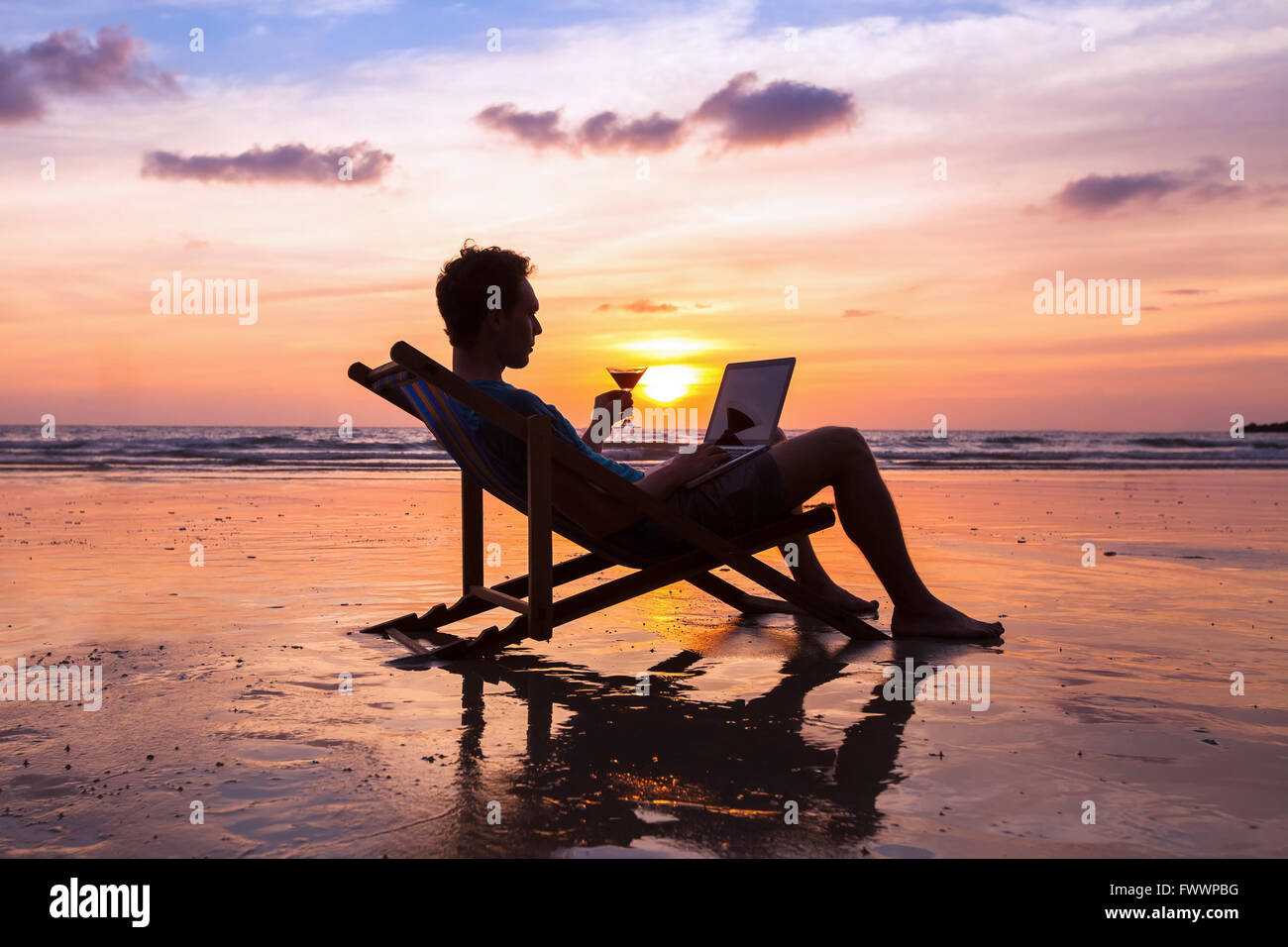 silhouette of successful business man reading emails on laptop on the beach at sunset, freelance job concept, work abroad Stock Photo