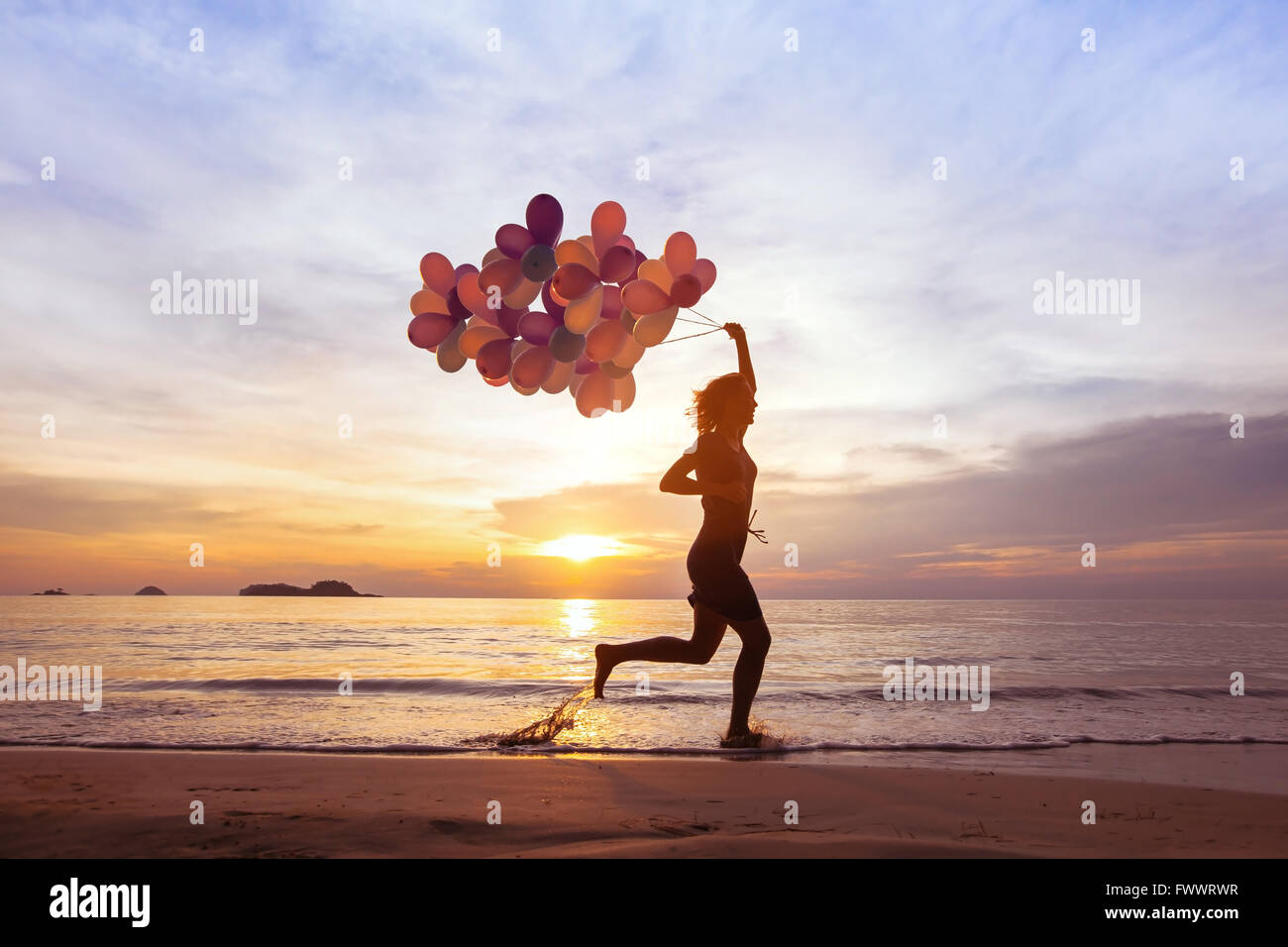 happiness concept, psychology of happy people, young woman running with multicolored balloons on the beach Stock Photo