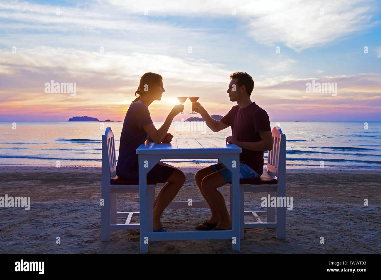 romantic dinner on the beach in luxury restaurant, couple on honeymoon drinking tropical cocktails at sunset Stock Photo