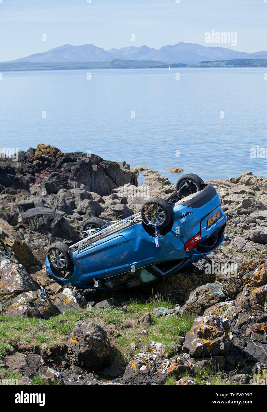 An overturned car crashed on rocks by the sea. Stock Photo