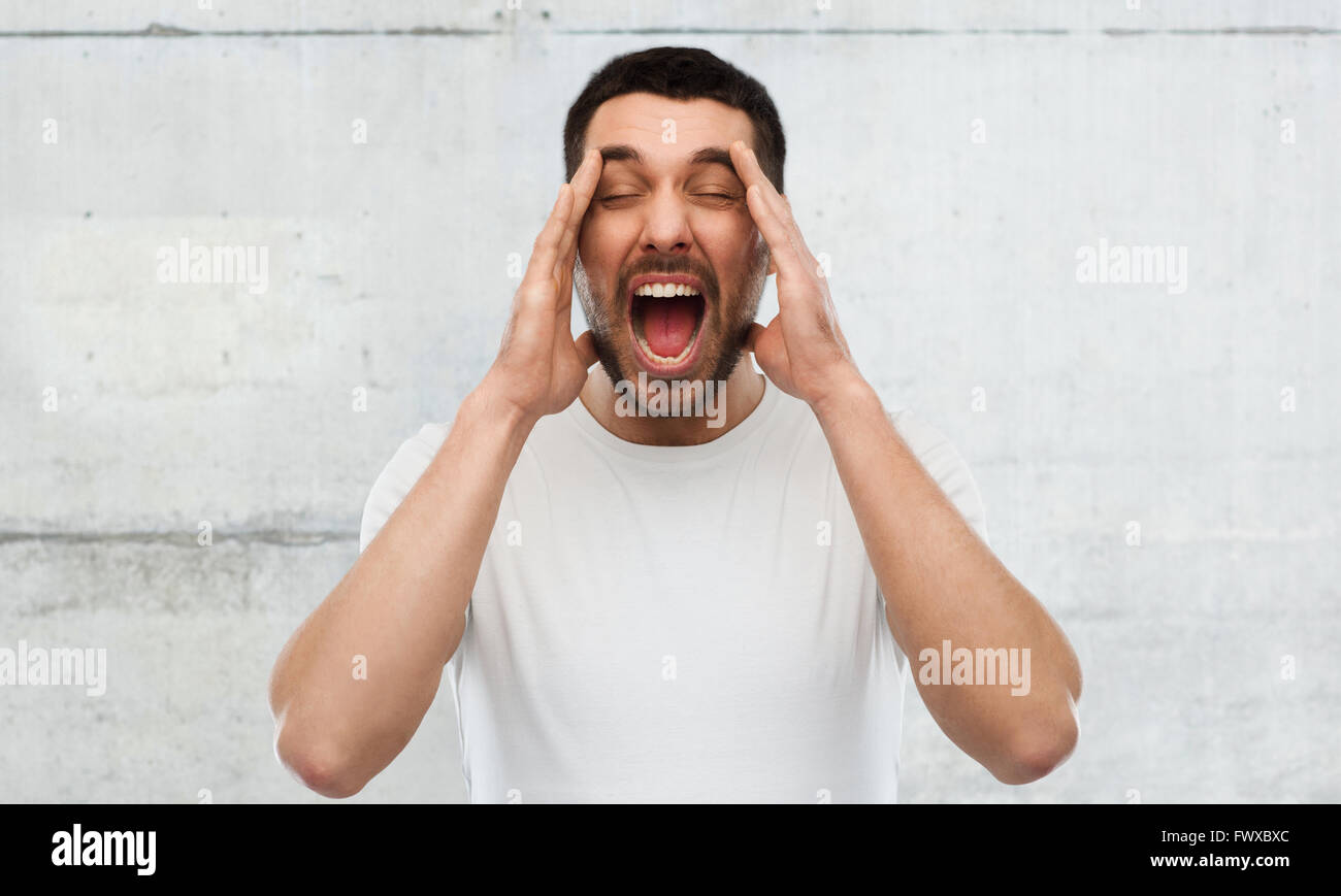crazy shouting man in t-shirt over gray wall Stock Photo