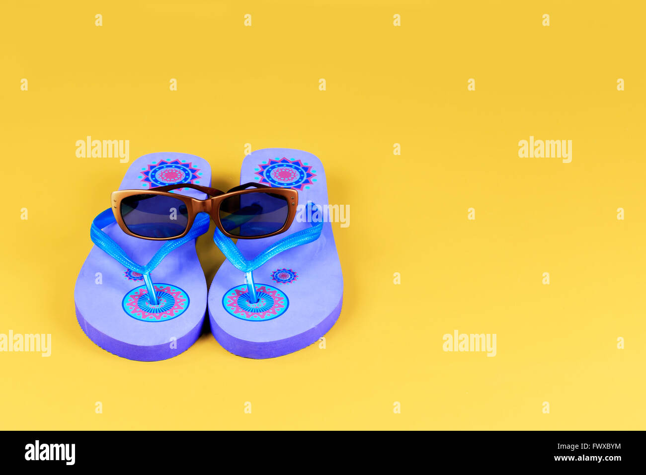 Pair of blue flip-flops and sun glasses on yellow background Stock Photo