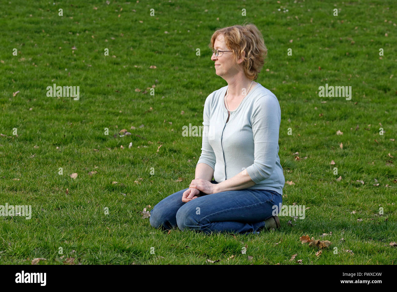 woman cowering on the lawn in a park Stock Photo