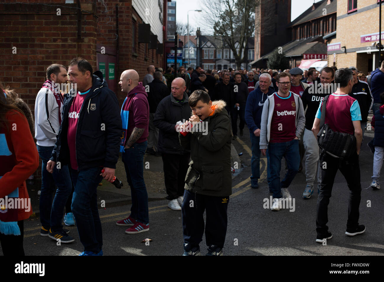 Fans making their way towards the ground along Castle Street at the Boleyn Ground before West Ham United hosted Crystal Palace in a Barclays Premier League match. The Boleyn Ground at Upton Park was the club's home ground from 1904 until the end of the 2015-16 season when they moved into the Olympic Stadium, built for the 2012 London games, at nearby Stratford. The match ended in a 2-2 draw, watched by a near-capacity crowd of 34,857. Stock Photo