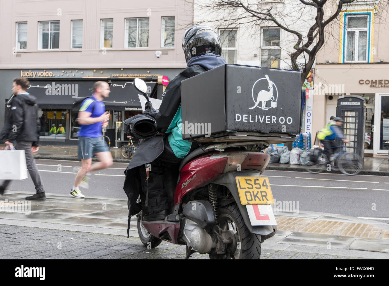 L-plated Deliveroo scooter delivery driver waiting for next delivery in London, UK Stock Photo