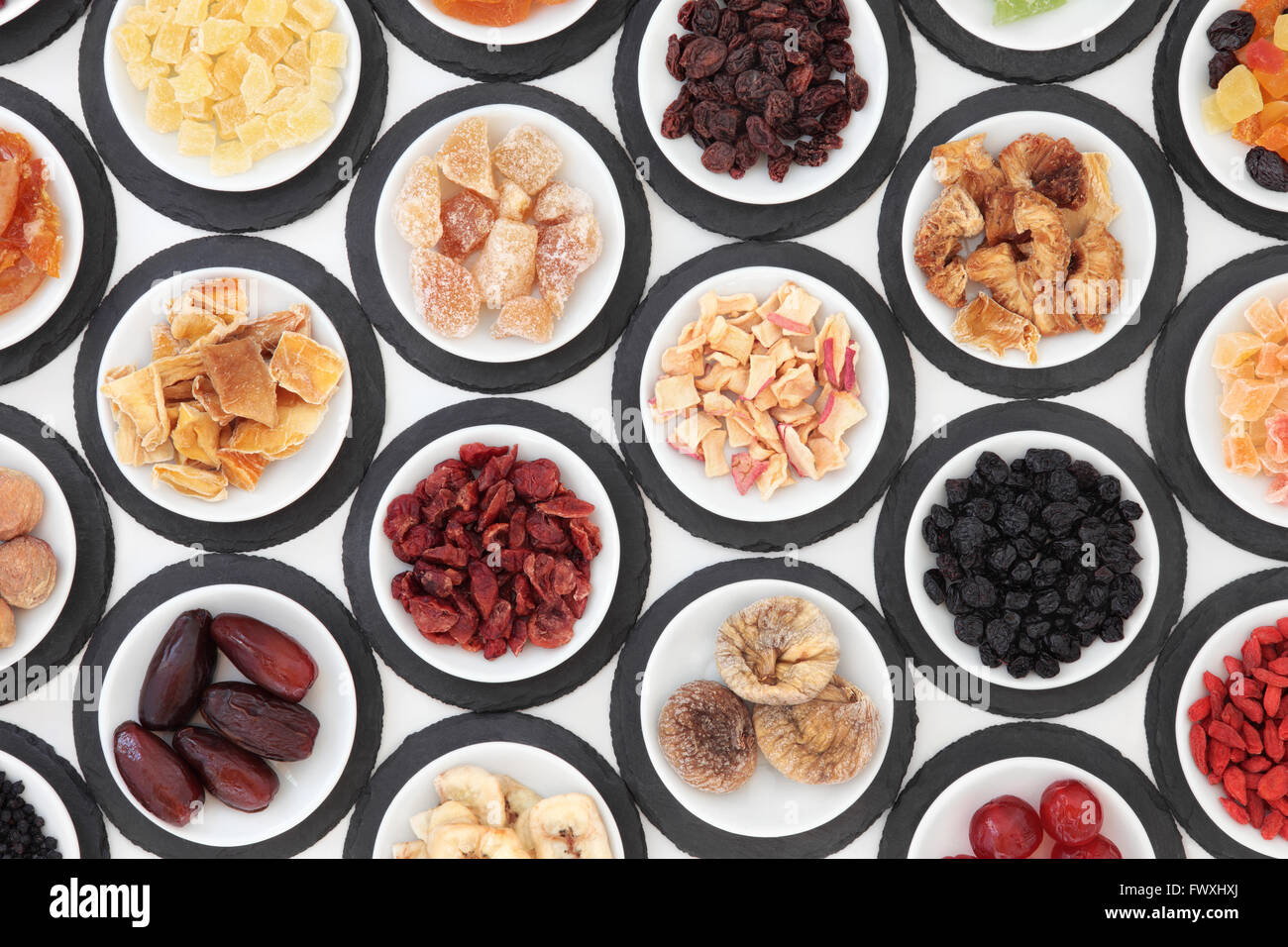 Dried fruit selection in porcelain bowls on slate rounds over white background. Stock Photo