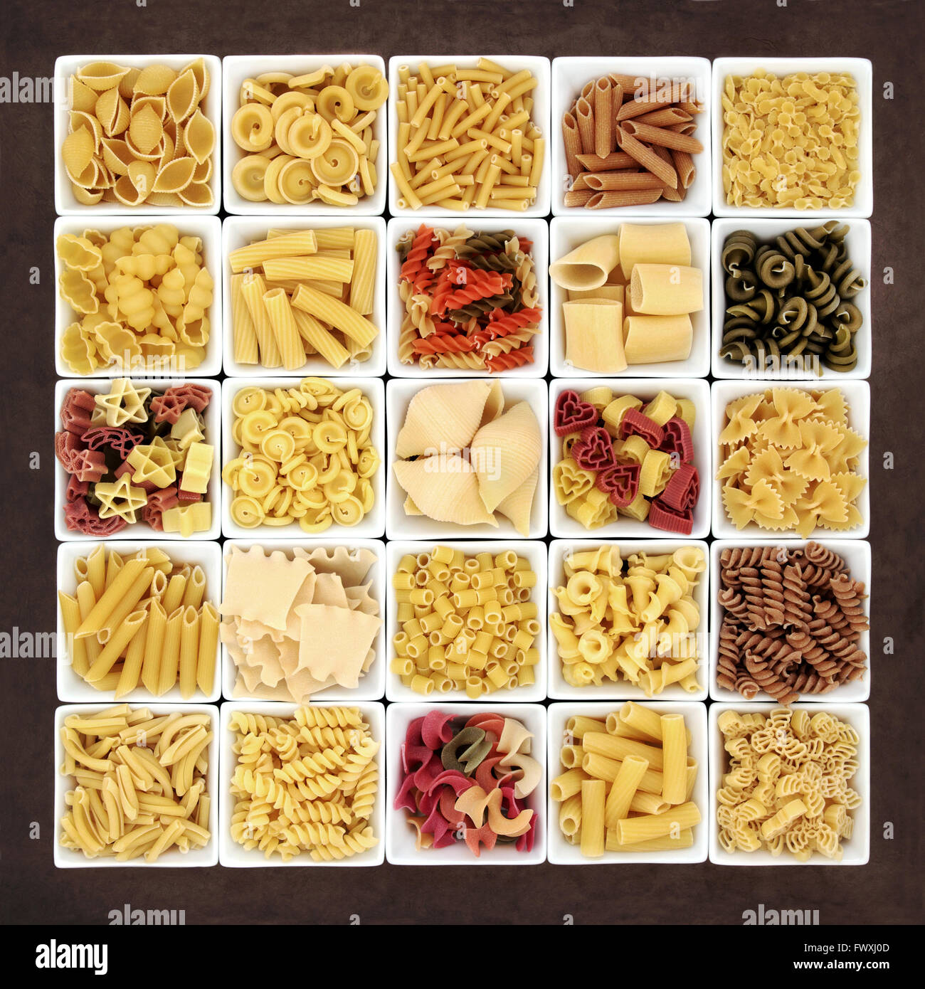 Large pasta dried food sampler in square dishes over brown lokta paper background. Stock Photo
