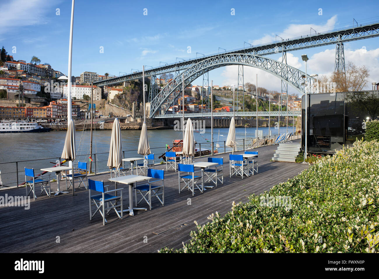 Outdoor cafe tables on riverside boardwalk at Douro river and Dom Luis I Bridge in Porto and Gaia, Portugal Stock Photo