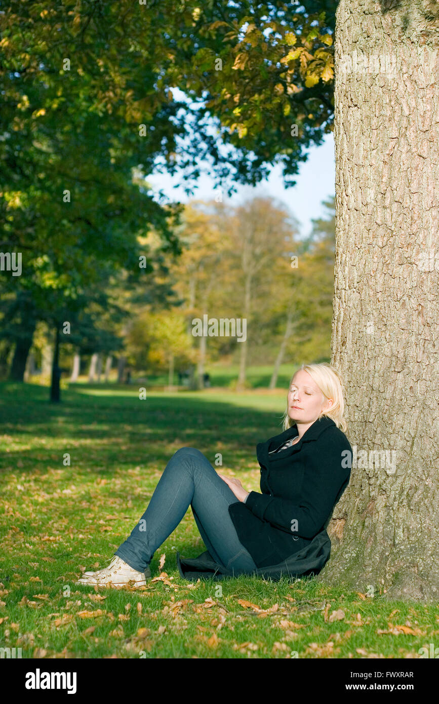 Woman sitting with eyes closed by tree in park Stock Photo - Alamy