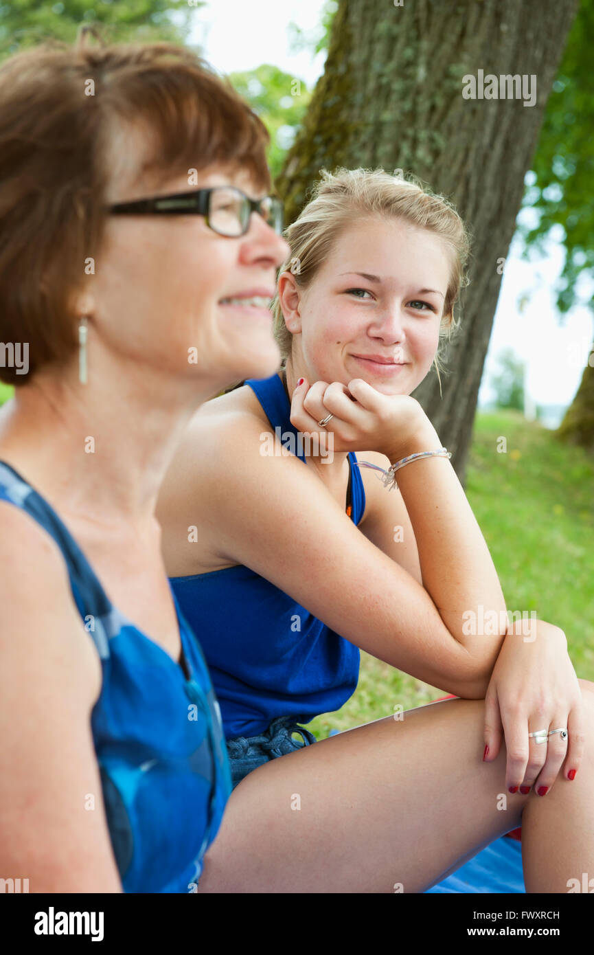 Sweden, Ostergotland, Grandmother and granddaughter sitting side by side on grass Stock Photo