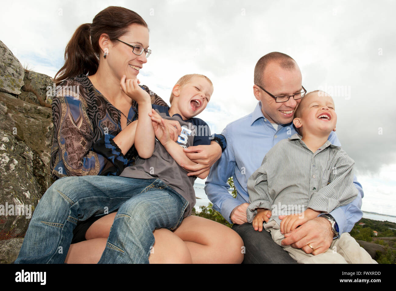 Sweden, Vastra Gotaland, Torslanda, Family with two children (4-5) sitting on rock Stock Photo