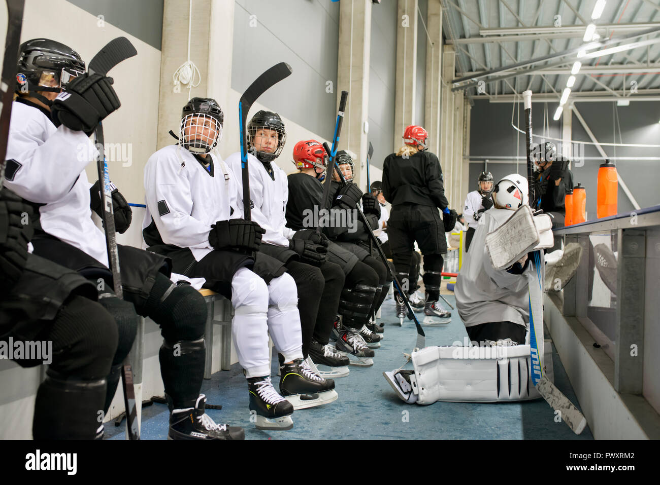 Sweden, Young ice hockey players sitting on bench by ice rink waiting