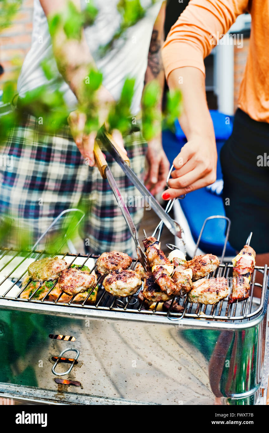 Sweden, Uppland, Danderyd, Couple grilling meat on barbecue Stock Photo