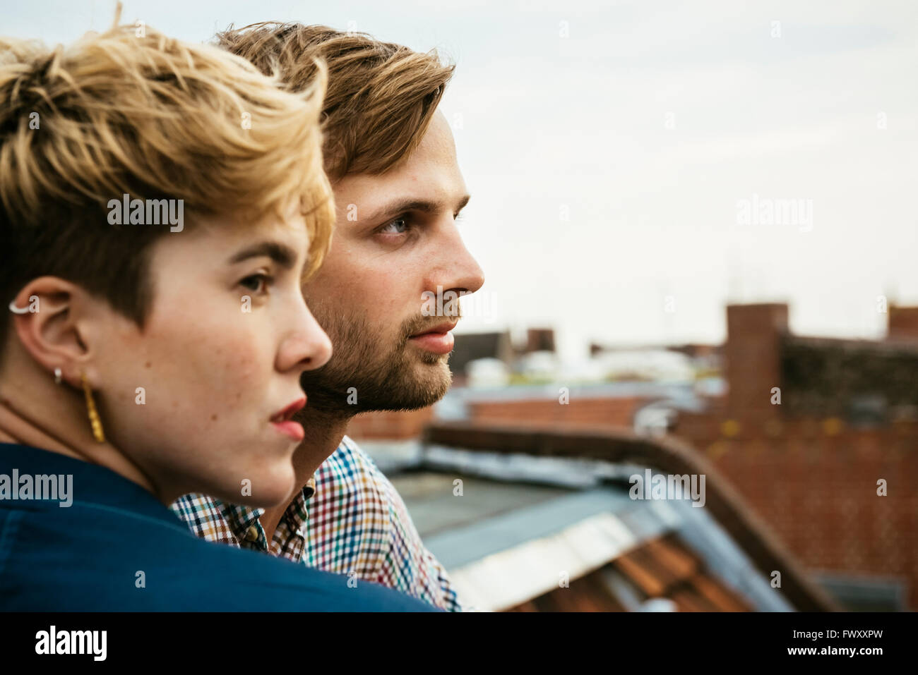 Germany, Berlin, Young couple side by side on rooftop against sky Stock Photo