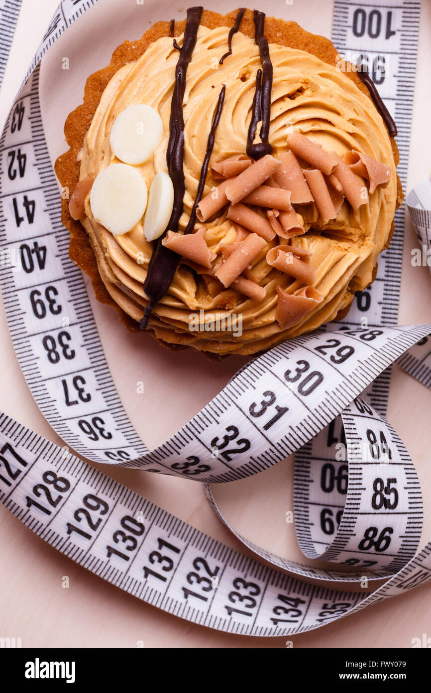 Appetite and gluttony concept. Fattening problem. Cake cupcake with measuring tape on table Stock Photo
