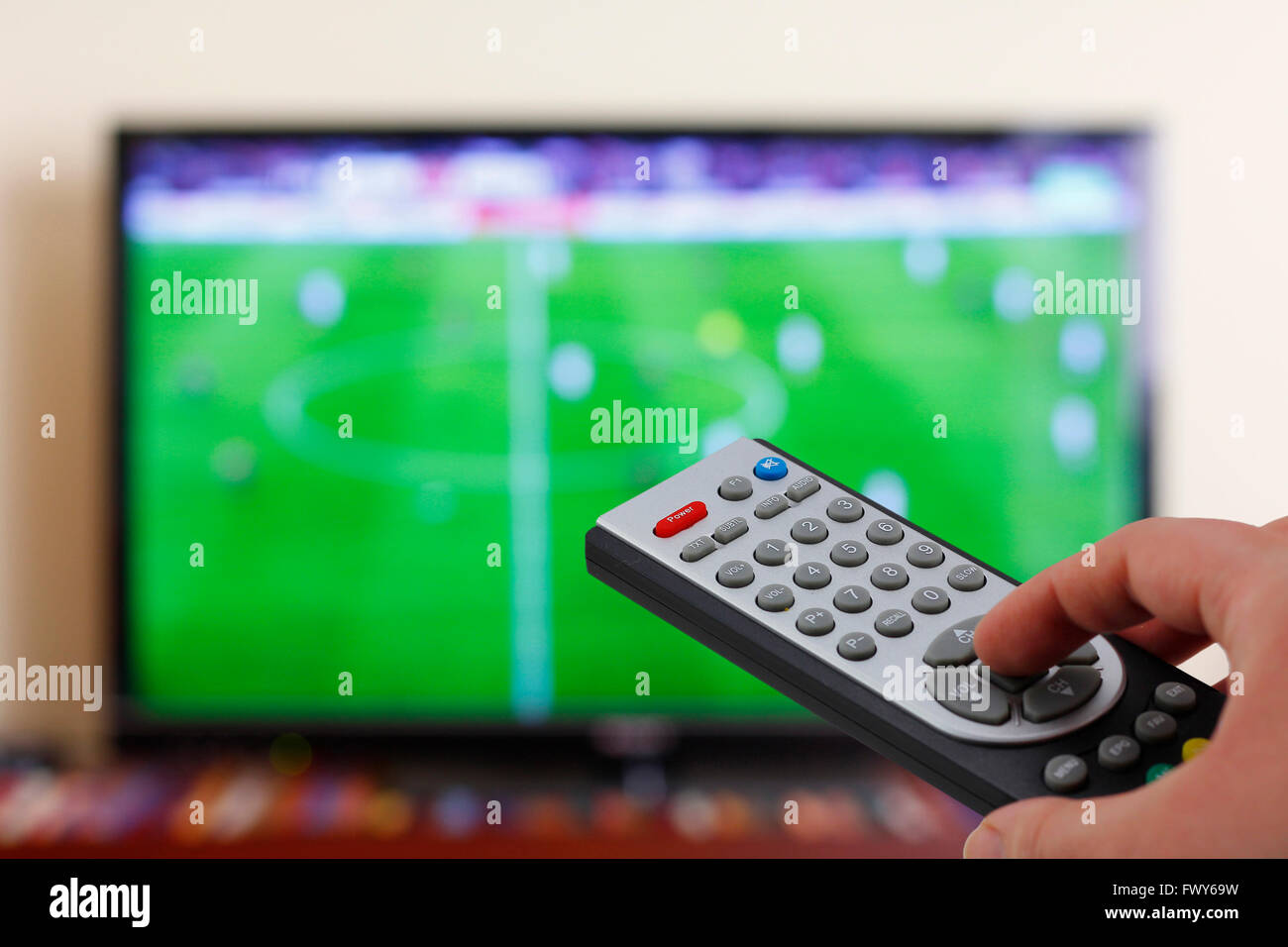 Watching a football match in the television, with a tv remote control in the hand Stock Photo
