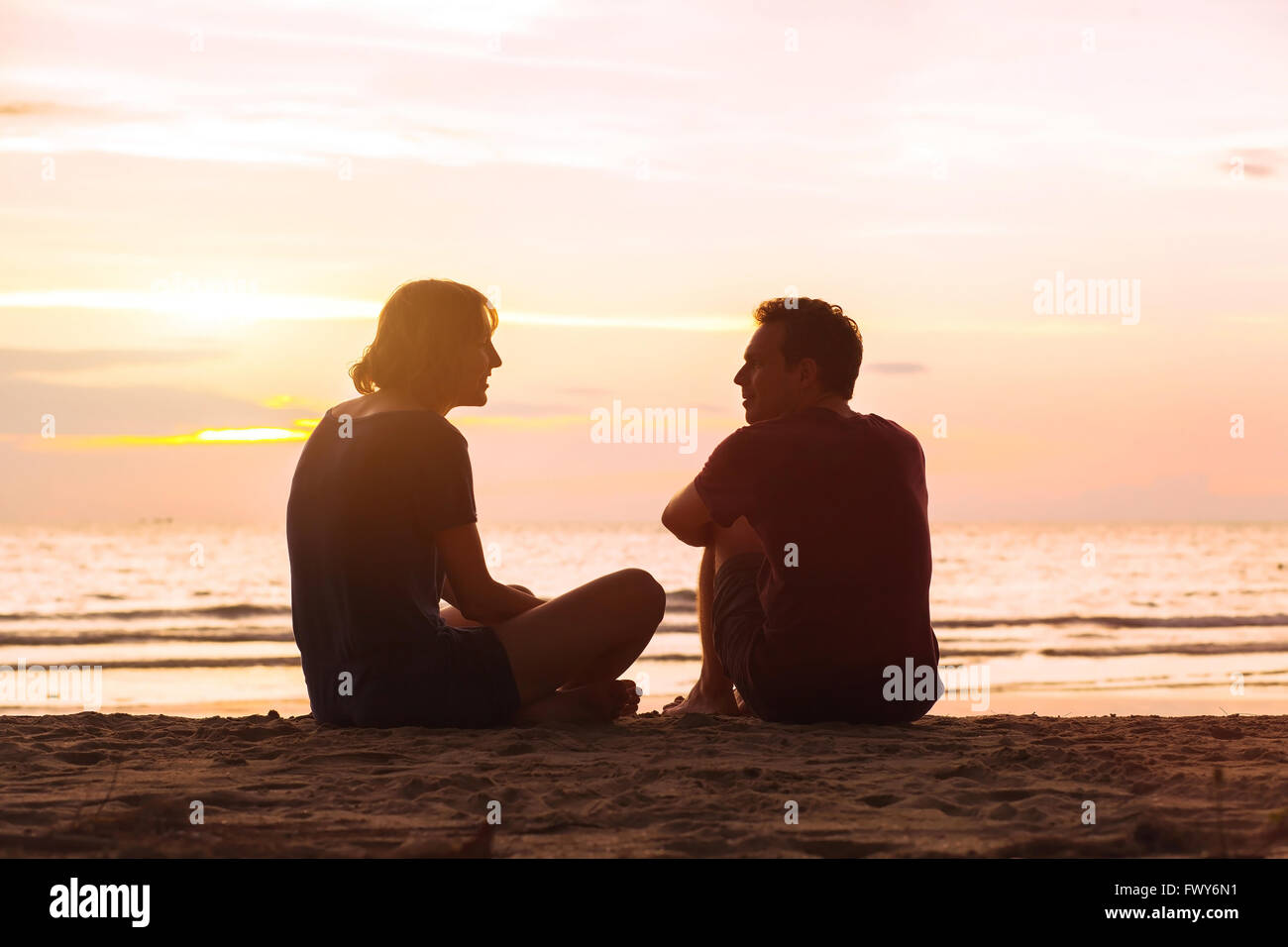 man and woman on the beach at sunset, young couple talking near the sea, dating or friendship concept Stock Photo