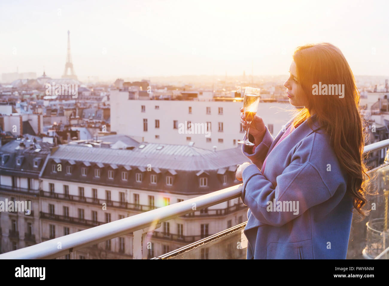 woman enjoying panoramic view of Paris and Eiffel tower at sunset, holding glass of wine or champagne in rooftop luxury restaura Stock Photo