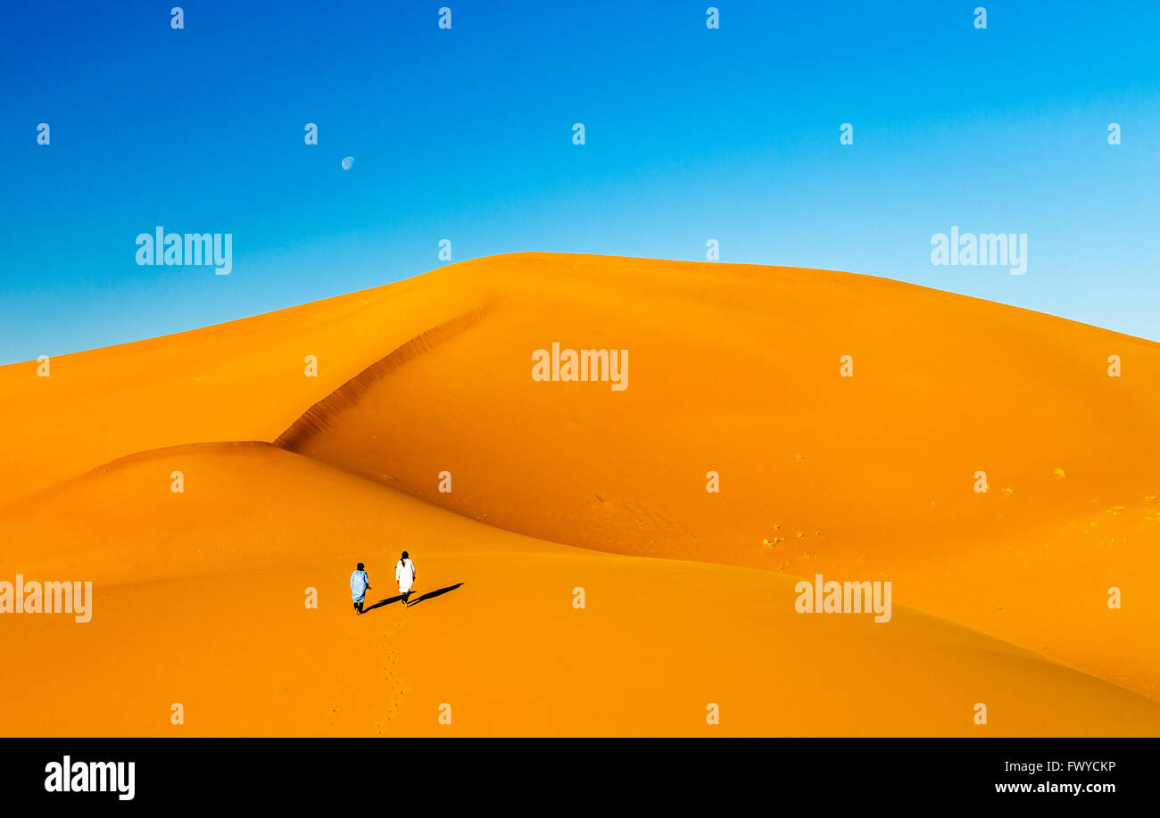 Two lonely Bedouins in the Sahara desert dunes of Erg Chigaga with the moon rising Stock Photo