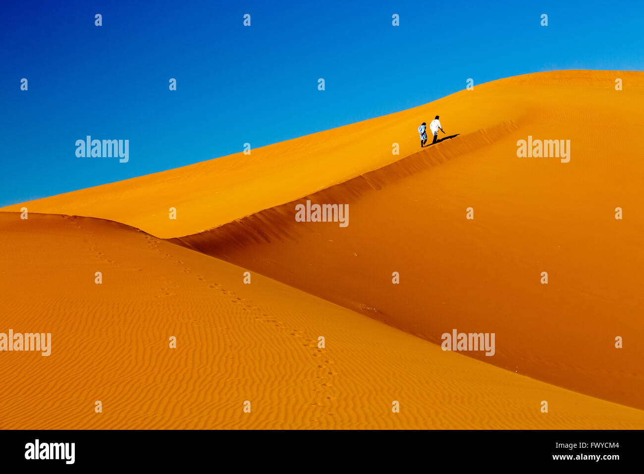 two Bedouins climbing Erg Chigaga dunes in Morocco Stock Photo
