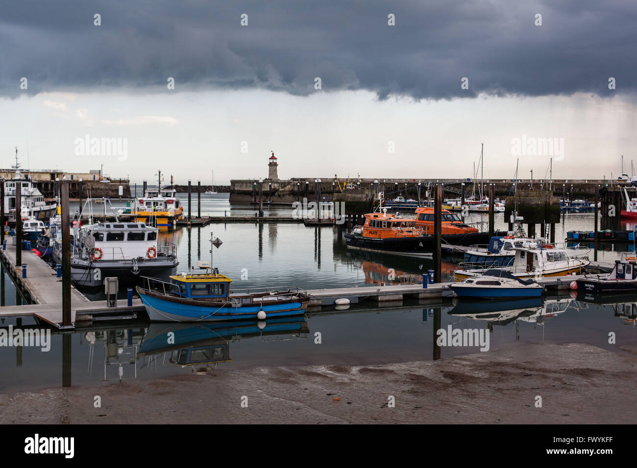 Very dark clouds approaching seaside harbour with boats Stock Photo