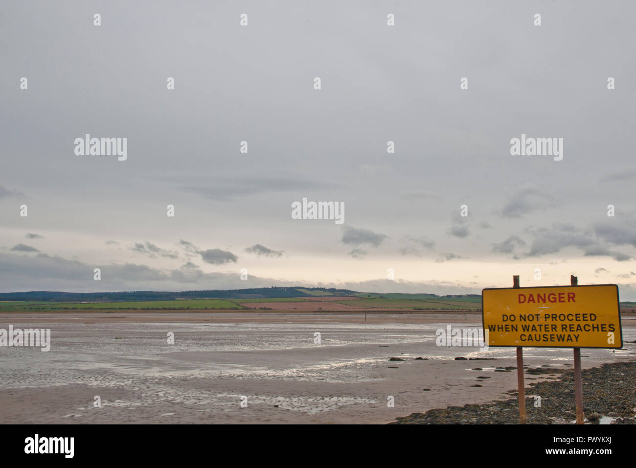 The uncovered causeway across from Lindisfarne (Holy Island)  to mainland at low tide, Northumberland, England with sign warning Stock Photo