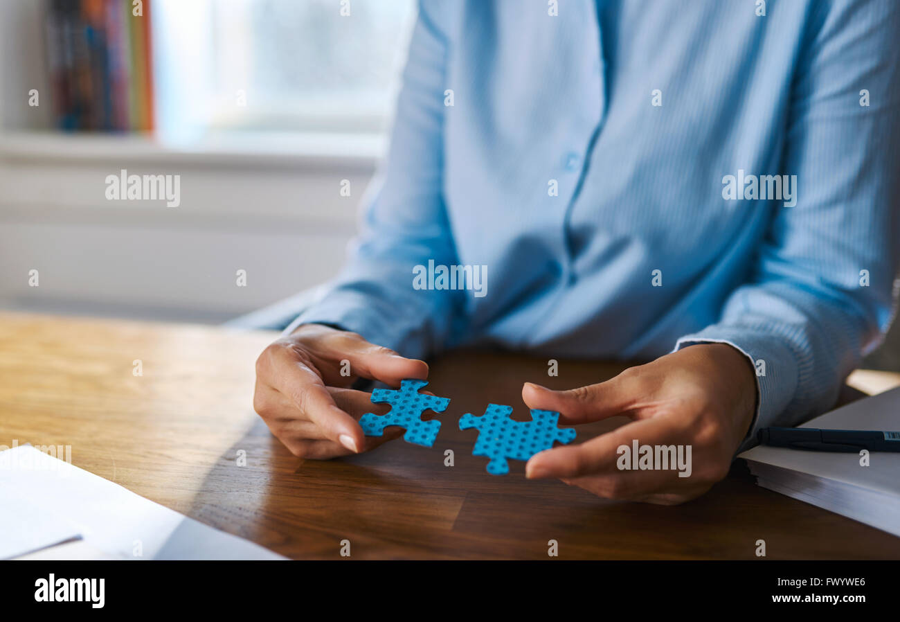 Cropped view close up of female hands at desk assembling two blue jigsaw puzzle pieces for concept about self employed people so Stock Photo