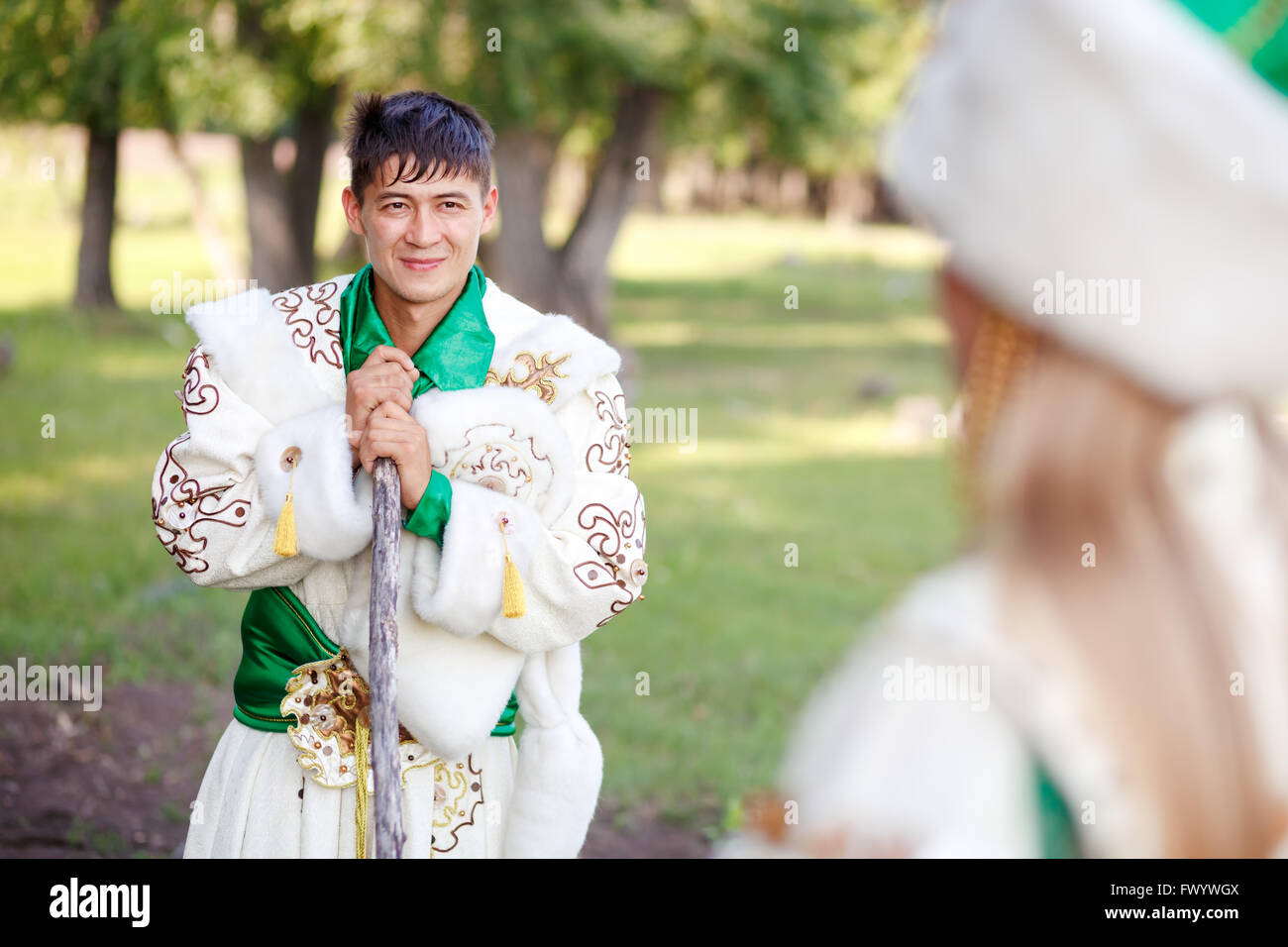 Man in traditional festive dress of steppe nomads, leaned on his cane, looking at wife. Stock Photo